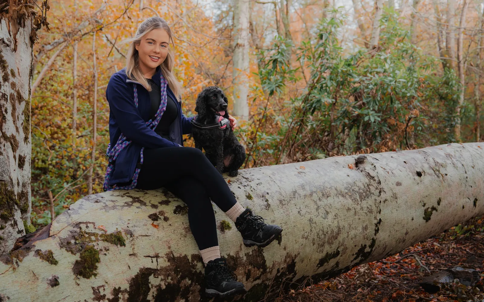Carly sitting on a fallen birch with her cocker spaniel in autumn woodland
